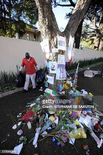 Housekeeper removes flowers and well wishing messages left for former South African President Nelson Mandela outside his house on July 1, 2013 in...