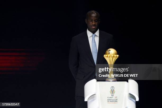 Former Ivorian footballer Yaya Toure stands on the stage next to the trophy during the Africa Cup of Nations 2024 official draw at Parc des...