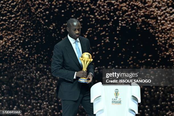 Former Ivorian footballer Yaya Toure puts the trophy on stage during the Africa Cup of Nations 2024 official draw at Parc des Expositions in Abidjan,...