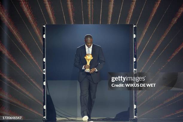 Former Ivorian footballer Yaya Toure brings the trophy on stage during the Africa Cup of Nations 2024 official draw at Parc des Expositions in...