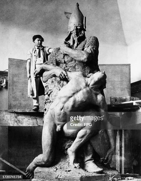 Hungarian sculptor Janos Pasztor, wearing a beret and a smock, stands on an elevated platform beside a statue depicting the Hungarian chieftain...