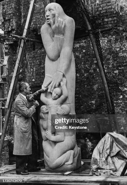 British sculptor and artist Edward Bainbridge Copnall, holding a mallet and chisel, as he works on 'The Word', a representation of a mother, father...