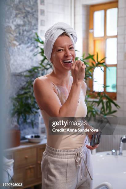 young woman with a white towel on the head brushes teeth - body brushing stock pictures, royalty-free photos & images
