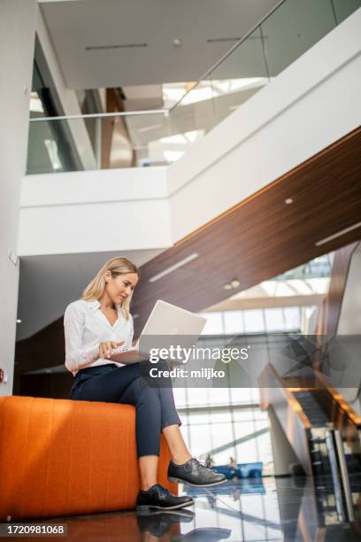 business woman sitting on sofa in the hall in office building and using laptop - star style lounge imagens e fotografias de stock