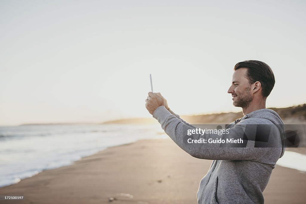 Smiling man taking pictures on beach.