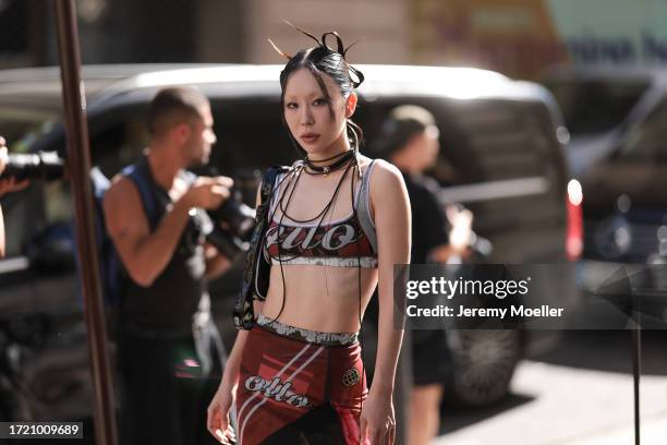 Mirani is seen wearing brown styled hair, a black bag, a red and dark bra and a matching red skirt from Ottolinger as well as several black chains...