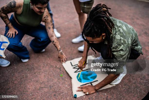 young man painting a poster during protest on the city - climate justice stock pictures, royalty-free photos & images