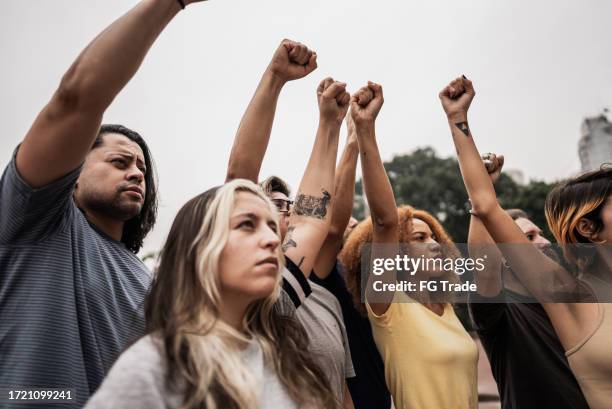 people with fist up during a protest at city street - civil rights stock pictures, royalty-free photos & images