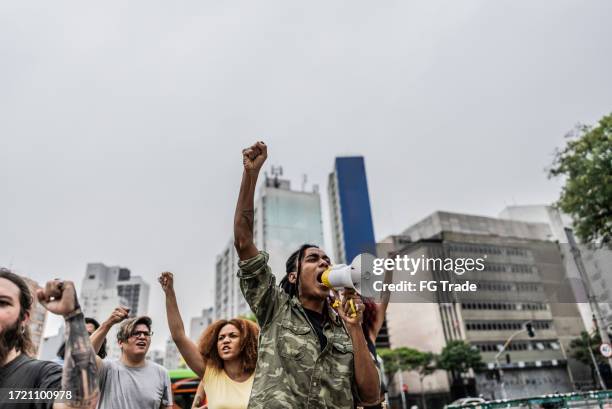 young man talking in a megaphone during a protest in the street - bürgerrecht stock-fotos und bilder