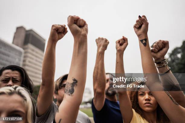 people with fist up during a protest at city street - street riot stock pictures, royalty-free photos & images