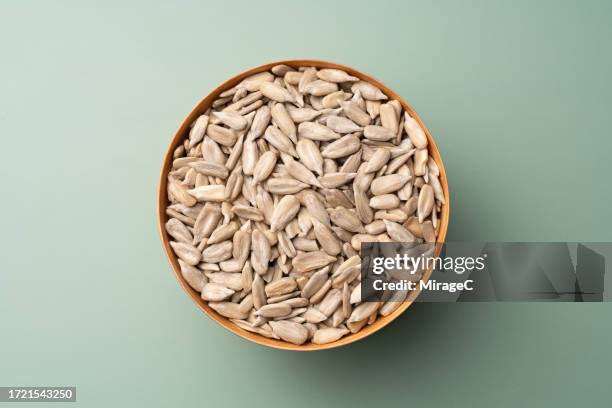 shelled sunflower seeds in wooden bowl on green background - semilla de girasol fotografías e imágenes de stock