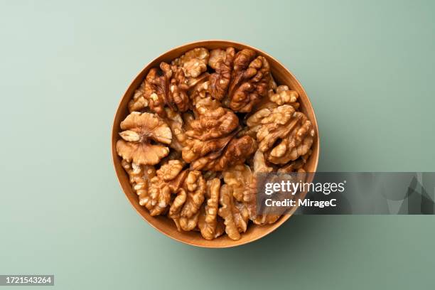 shelled walnuts in wooden bowl on green background - walnuss stock-fotos und bilder