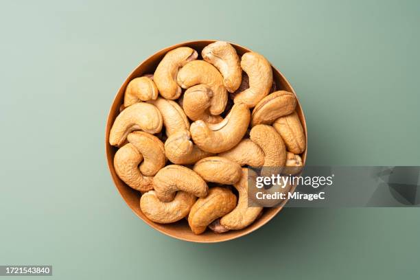 cashew nuts in wooden bowl on green background - cashew stock pictures, royalty-free photos & images