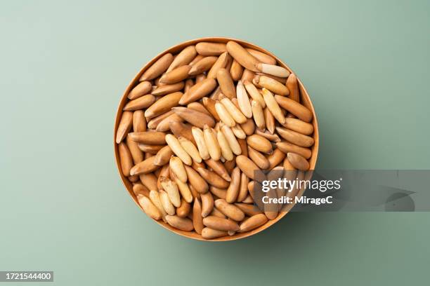 shelled chilgoza pine nuts in wooden bowl on green background - pinon stock pictures, royalty-free photos & images