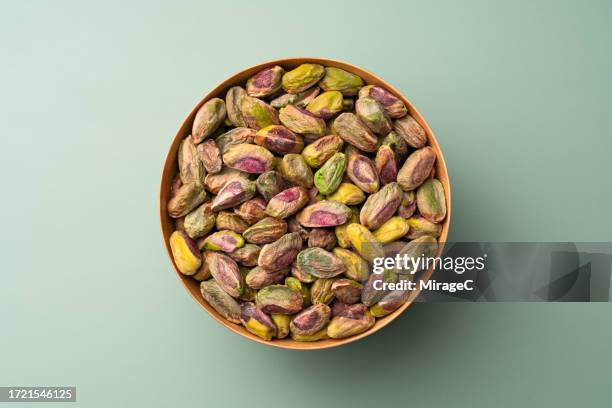 shelled pistachio nuts in wooden bowl on green background - pistacho fotografías e imágenes de stock