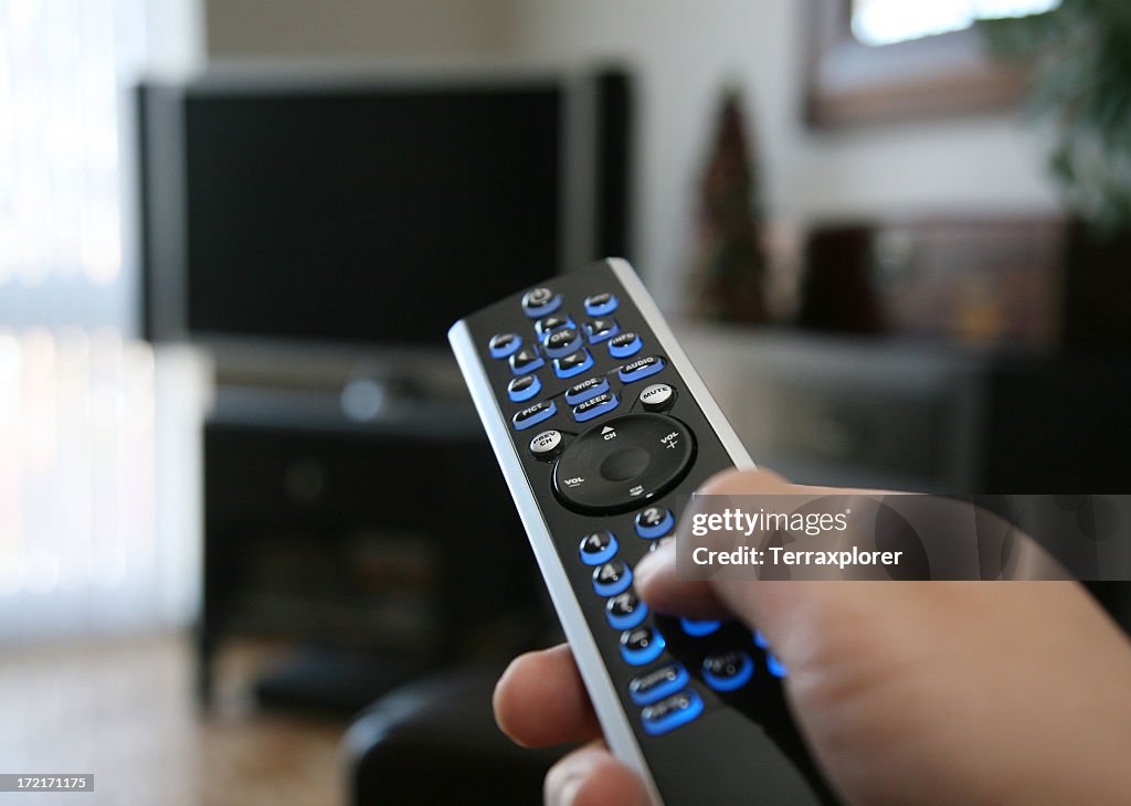 A hand pointing a remote control at the TV