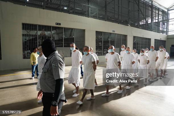 Gang members of the "Mara Salvatrucha" and "Barrio 18" are taken to their cells by a prison officer inside at CECOT on October 12, 2023 in Tecoluca,...