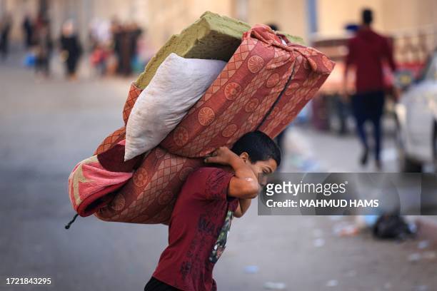 Boy carries a mattres as Palestinians with their belongings flee to safer areas in Gaza City after Israeli air strikes, on October 13, 2023. Israel...