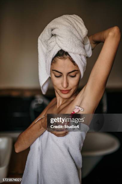 an elegant woman with a towel wrapped around her waist, meticulously shaving her underarms in her bathroom - oksel stockfoto's en -beelden
