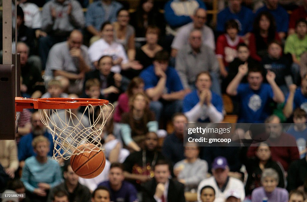 Basketball ball and backboard with fans in the background.