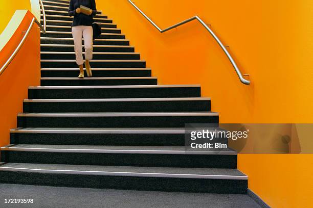 young woman walking down orange stairs, reading book - staircase stock pictures, royalty-free photos & images