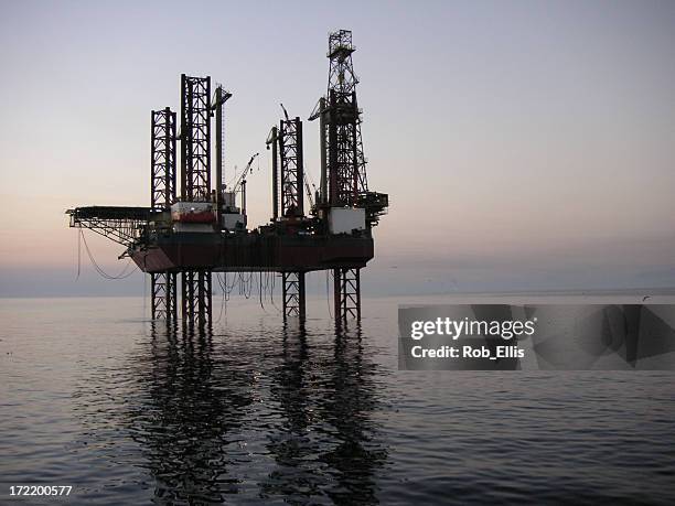 a distant shot of an oil rig at dusk - iran oil stock pictures, royalty-free photos & images