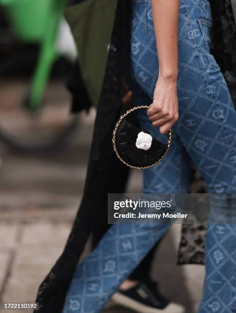 Guest is seen outside Chanel show wearing small round leather Chanel handbag with white camellia flower and Chanel denim logo pants during the...