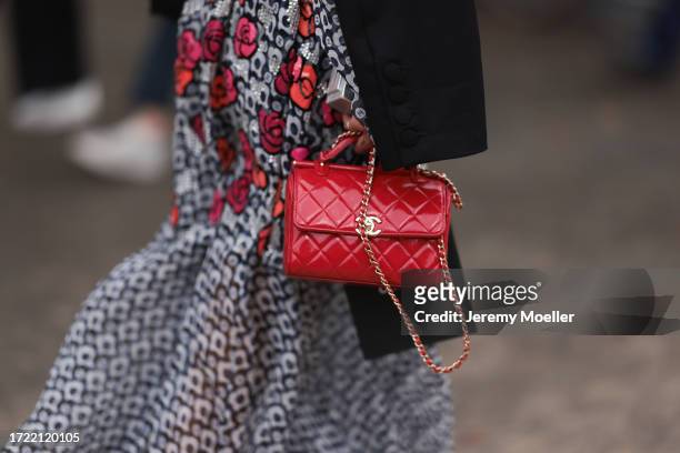 Guest is seen outside Chanel show wearing a black and white patterned Chanel dress with colorful camellia details, red leather Chanel handbag and...