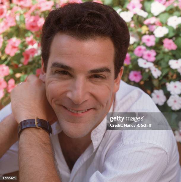 Portrait of American actor and singer Mandy Patinkin posing in front of a field of flowers, 1988.