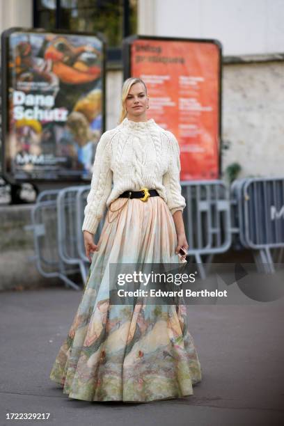 Guest wears a white knit pullover, a belt with golden buckle, a gathered pleated colored tie and dye long skirt, earrings, outside Zimmermann, during...