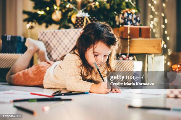 girl write a letter to santa claus in front of the christmas tree. - kinder schreiben stock-fotos und bilder