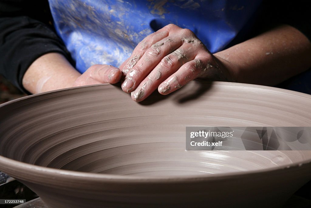 Potters hands shaping rim of clay bowl