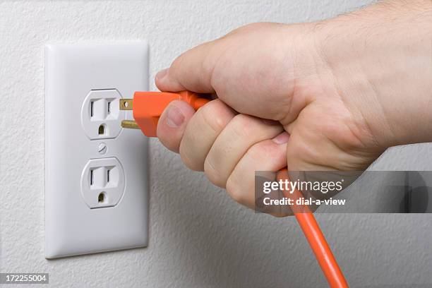 a hand unplugging an orange cord from a white outlet - electrical plug stock pictures, royalty-free photos & images