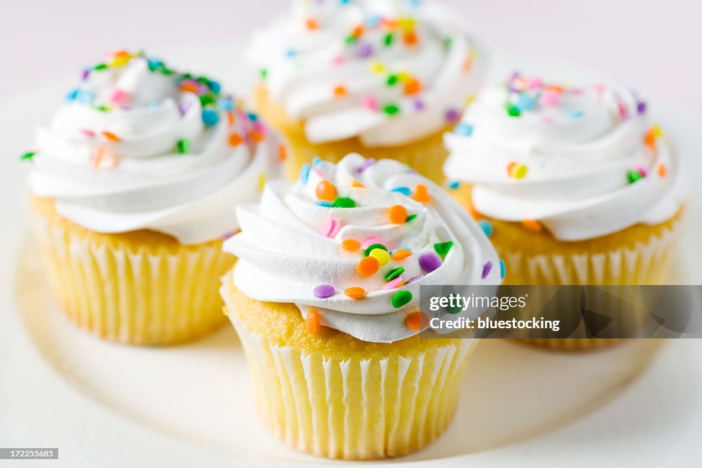 Four yellow cake and white frosted cupcakes with confetti