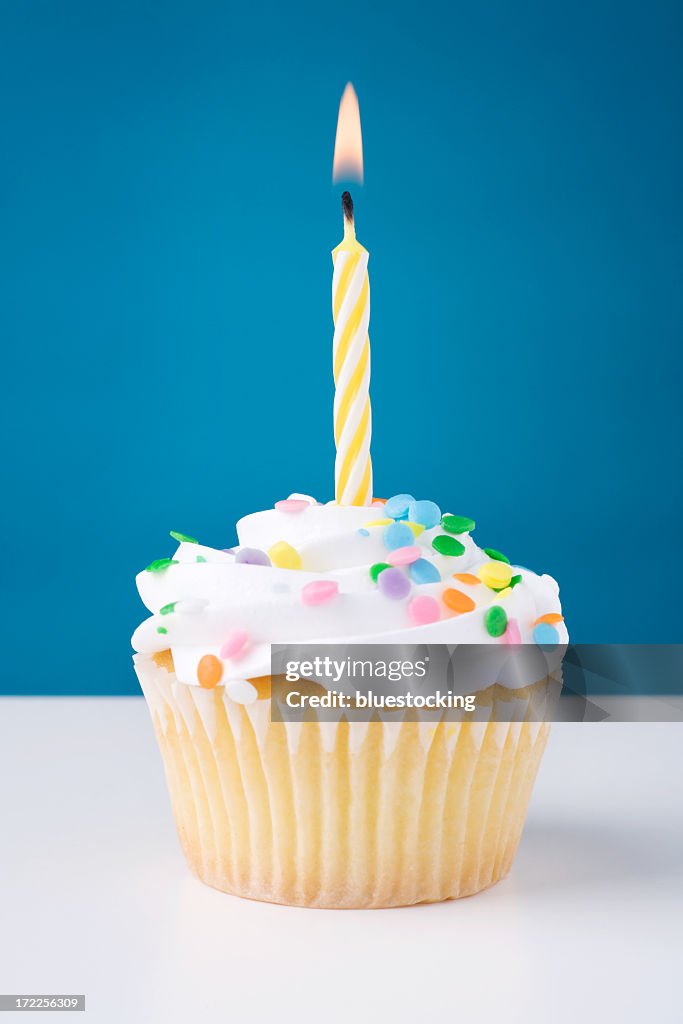 Birthday cupcake with white icing and sprinkles and candle