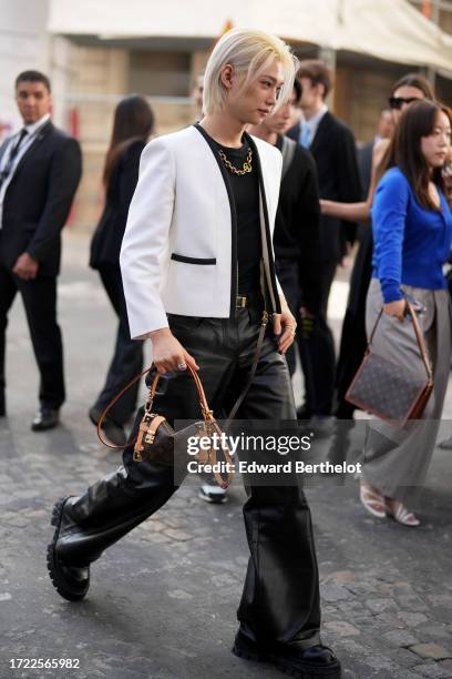 Felix wears a black top, a golden chain necklace, a white blazer jacket, a belt, leather pants, a brown monogram Vuitton bag, leather shoes, outside...