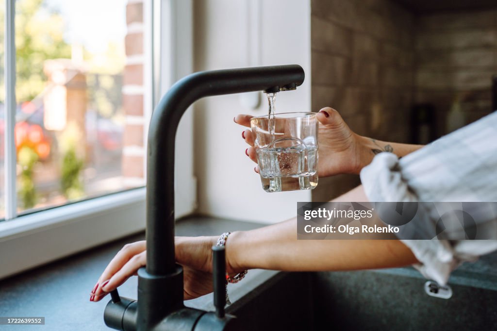 Water filtration in domestic kitchen. Unrecognizable woman hands pouring water in drinking glass from tap