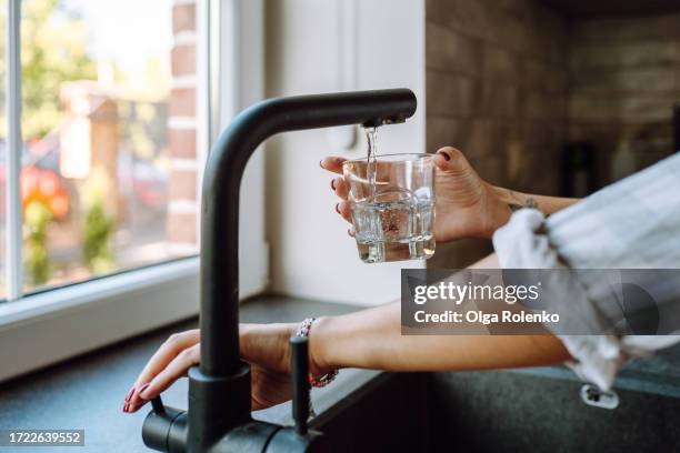 water filtration in domestic kitchen. unrecognizable woman hands pouring water in drinking glass from tap - desperdício de água imagens e fotografias de stock