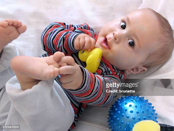 happy baby looking at the camera while playing with his toes - male feet on face stock pictures, royalty-free photos & images