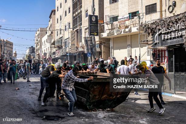Palestinian protesters push a dumpster to be used for cover during clashes with Israeli forces following a rally in solidarity with Gaza by...