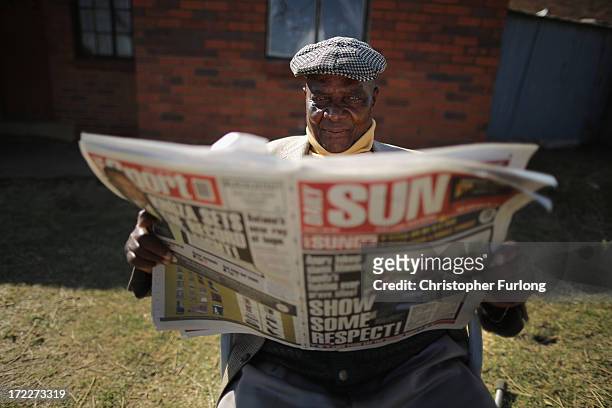 Man sits outside his Soweto home and reads the Daily Sun newspaper which headlines the Mandela family feud over grave sites on July 2, 2013 in...