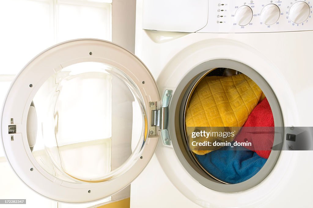 Close-up of washing machine, opened door, laundry inside, three towels