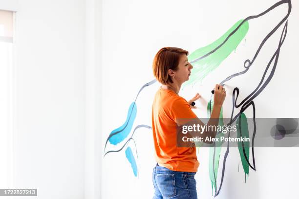 colorful mural project: red haired woman painting design whale on the wall in bright room - mural stock pictures, royalty-free photos & images