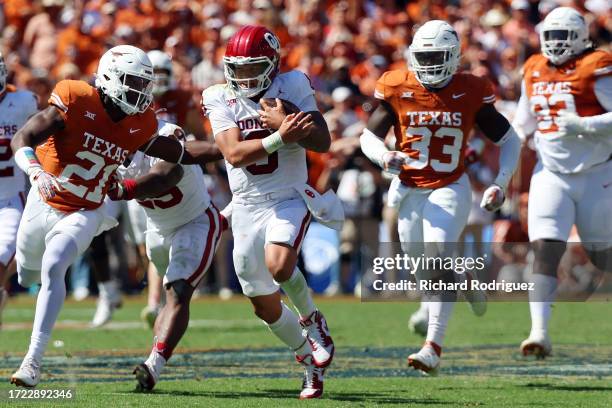 Quarterback Dillon Gabriel of the Oklahoma Sooners runs the ball as he is pursued by Kitan Crawford and David Gbenda of the Texas Longhorns at the...