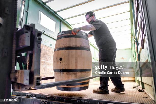 a worker in a cooperage in jerez (sherry) loads the barrels onto the truck for a scotch malt whiskey producer - wijnvat stockfoto's en -beelden