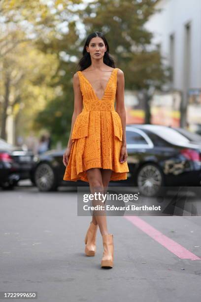 Guest wears an orange sleeveless low-neck gathered / pleated mini short dress, pastel colored platform boots, outside Zimmermann, during the...