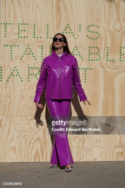 Guest wears sunglasses, a neon purple shiny vinyl jacket and matching flared pants, silver pointed shoes, outside Stella McCartney, during the...