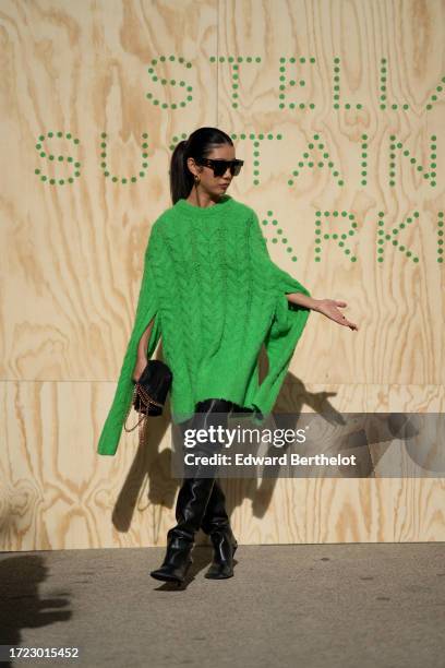 Guest wears sunglasses, a green wool knit oversized long pullover worn as a dress, black thigh high leather pointed boots, outside Stella McCartney,...