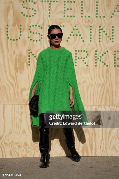 Guest wears sunglasses, a green wool knit oversized long pullover worn as a dress, black thigh high leather pointed boots, outside Stella McCartney,...