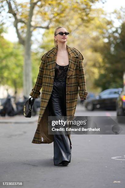 Guest wears sunglasses, a khaki checkered long coat, a black low neck floral embroidery mesh top, black flared leather pants, outside Zimmermann,...